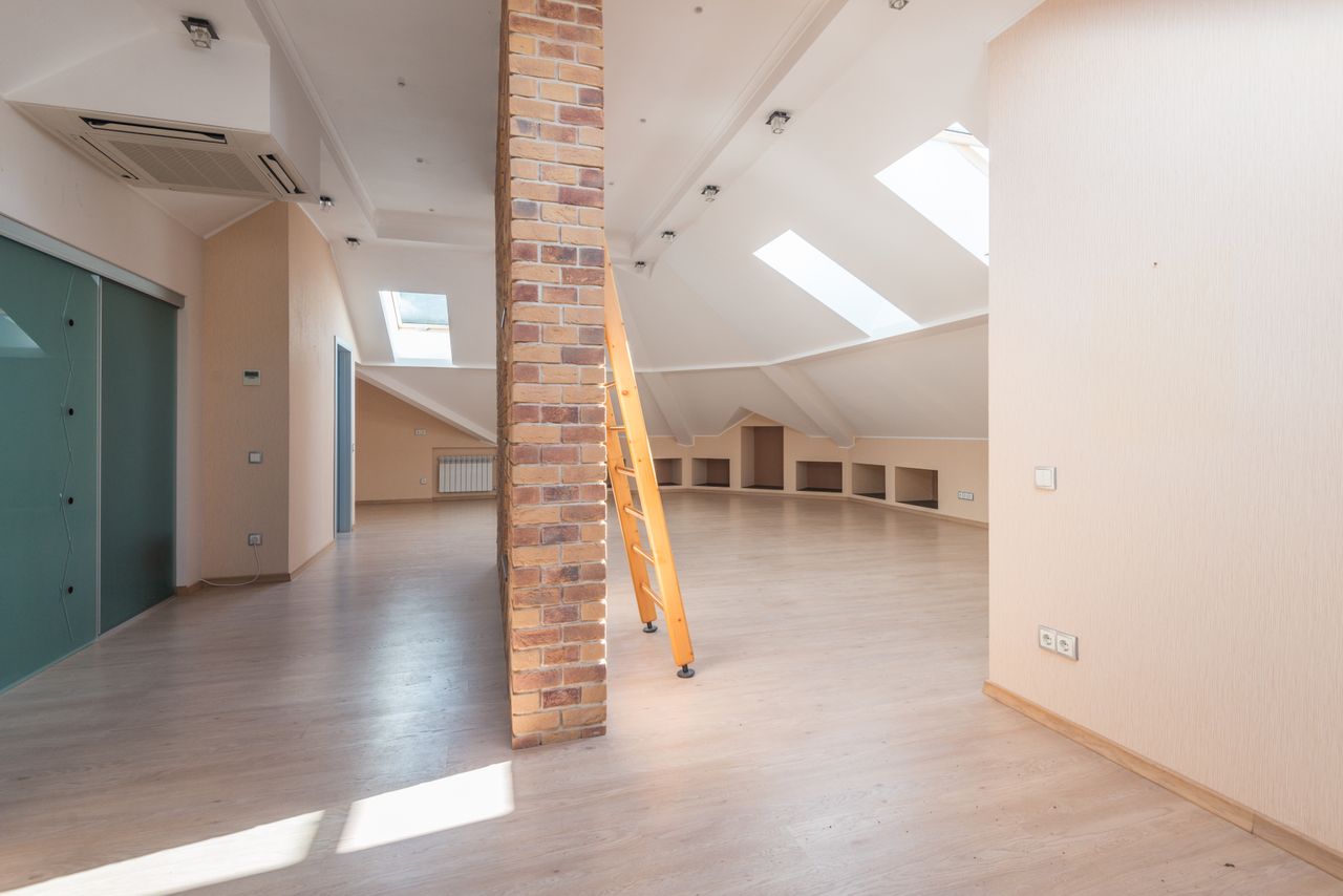 services-01 Spacious attic room with natural light from skylights, featuring a brick pillar and a wooden ladder.